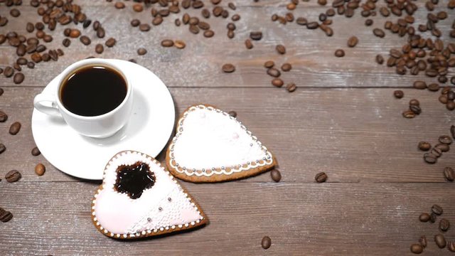 Food art. Good morning concept. cup of coffee and 2 heart-shaped gingersnaps are on wooden background. Coffee beans fall down in slow motion