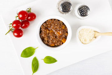 Sauce Bolognese, Parmesan cheese, a branch of tomatoes. Basil and spices. In a white plate. The background is white. Italian food. Copy space. Top view. Horizontal shot.