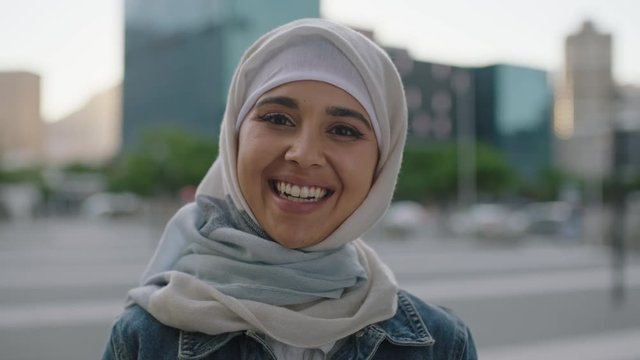 portrait of young independent muslim woman looking at camera smiling cheerful wearing hijab headscarf in urban city at sunset