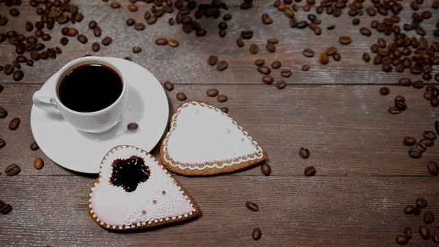 Food art. Good morning concept. cup of coffee and 2 heart-shaped gingersnaps are on wooden background. Coffee beans fall down in slow motion