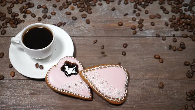 Food art. Good morning concept. cup of coffee and 2 heart-shaped gingersnaps are on wooden background. Coffee beans fall down in slow motion