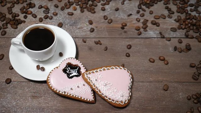 Food art. Good morning concept. cup of coffee and 2 heart-shaped gingersnaps are on wooden background. Coffee beans fall down in slow motion
