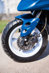 Fototapeta premium Front wheel of blue modern scooter on the gravel road