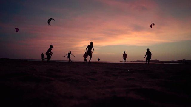 Children playing football (soccer) on the beach during sunset