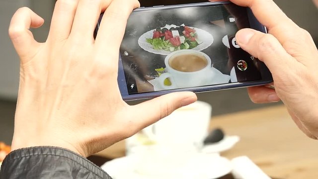 woman in outdoor cafe takes a picture of food green salad and cup of coffee. slow motion