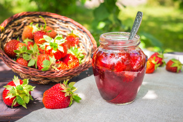 Strawberry jam and juicy ripe strawberries on a wooden table in the garden on a summer sunny afternoon in a rustic style, the concept of gardening, healthy organic vitamin nutrition
