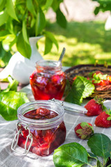 Strawberry jam and juicy ripe strawberries on a wooden table in the garden on a summer sunny afternoon in a rustic style, the concept of gardening, healthy organic vitamin nutrition