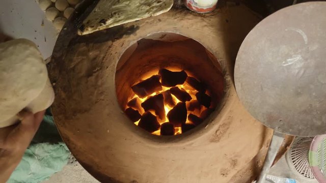 Baker making turkish pita bread in tandoor, clay oven. Baking process.