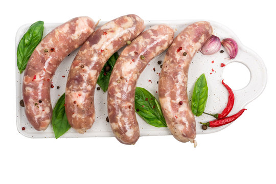 Raw sausages on white cutting board with basil and spices isolated on white background.