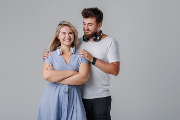 Young cheerful and cheerful couple with wireless headphones, smiling against a gray background. Club DJs