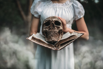 Female victim holds book and human skull in hand