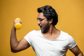 Indian man shows his muscle while holding yellow dumbbell in hand. boast with strong arms and good...