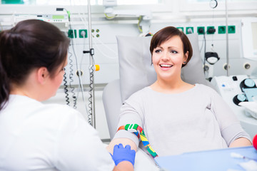 Nurse in hospital checking access at happy woman blood donor