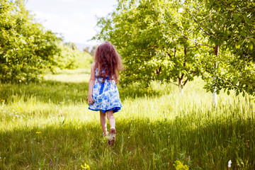 little girl in a dress with blue flowers runs in the meadow and rejoices