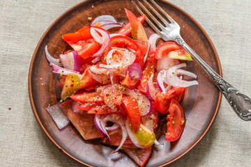 Delicious simple salad of tomato and red onion on a rustic pottery plate