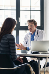 Obraz premium Young devoted doctor holding an X-ray while listening with attention to his female patient during a private consultation in the office