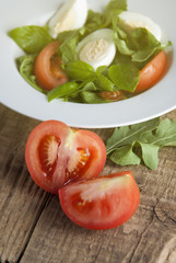 Fresh tomatoe slices over plate of green health salad wooden rustic background. diet, fitnes and healthy food concept.
