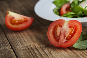 Fresh tomatoe slices over plate of green health salad wooden rustic background. diet, fitnes and healthy food concept.