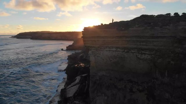 Man walking down a cliff with the sun setting in the background.