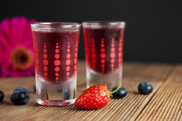 Red berries liqueur in shot glass isolated on black background and wooden table. Homemade alcohol drink concept.