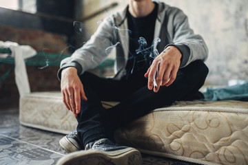 Junkie sitting on the mattress and smoke cigarette