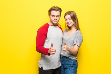 Two smiling happy couple showing thumbs-up on yellow background