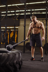 a serious sportsman with a sledgehammer is preparing to hit the tire at the gym sport and bodybuilding concept