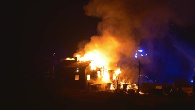 Burning house, firefighters and arriving fire truck in the background.