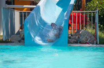 boy on water slide with splashing water by the pool