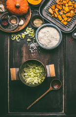 Ingredients of tasty pumpkin dish with rice in cooking pot on dark rustic kitchen table background, top view. Pumpkin risotto preparation .   Autumn seasonal rustic country food