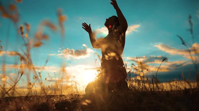 woman praying on her knees. Girl folded her hands in prayer silhouette at sunset. slow motion video. Girl folded her hands in prayer pray to God. the girl praying asks forgiveness for lifestyle sins
