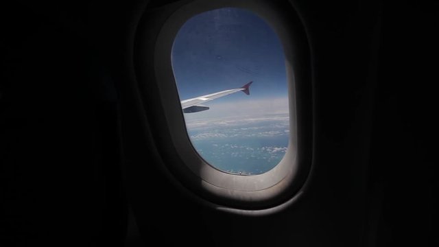View of the blue sky and clouds through the window of the aircraft, Close up Airplane window with airplane wing, Traveling concept