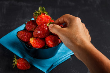 A tanned woman's hand takes the strawberries from the plate. The concept of healthy eating.