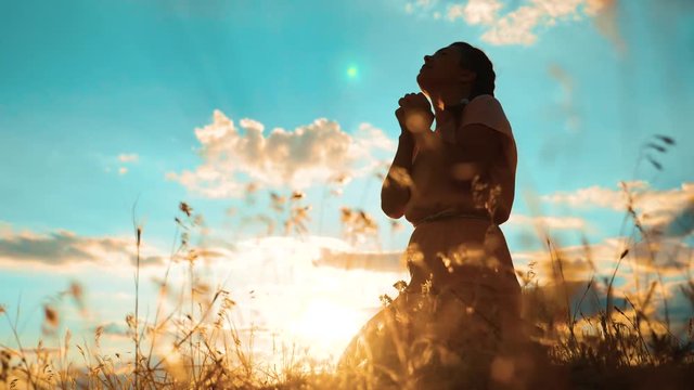 Girl folded her hands in prayer silhouette at sunset. woman praying on her knees. slow motion video. Girl folded her hands in prayer pray to God. the girl praying asks forgiveness for sins of