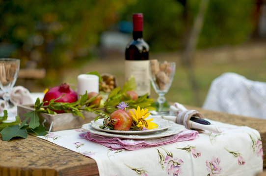 Lunch is romantic in autumn garden, atmosphere of holiday and coziness. Autumnal dinner in the open air with wine and fruit. Decor table with flowers and pomegranate. Vintage photo