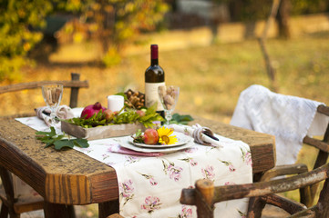 Romantic dinner in the autumn garden, table setting for a nice dinner. Wine, fruit, pomegranate and...