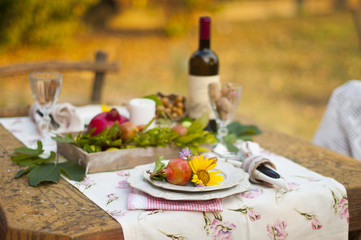 Romantic dinner in the autumn garden, table setting for a nice dinner. Wine, fruit, pomegranate and flowers. Picnic in the open air