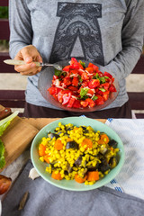 Woman hands holds vegetarian lunch with fresh red tomatoes and salad leaves, cooked vegetables, boiled corn grain, eggplants, carrots. Vegan dinner and healthy food