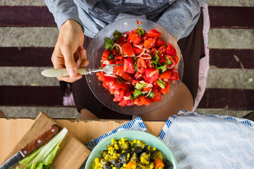 Woman hands holds vegetarian lunch with fresh red tomatoes and salad leaves, cooked vegetables, boiled corn grain, eggplants, carrots. Vegan dinner and healthy food