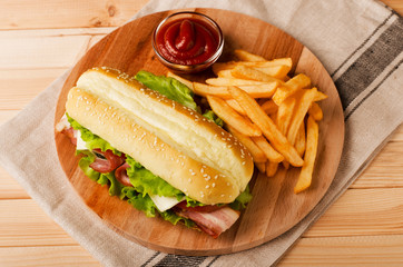 Fresh submarine sandwich with ham, cheese, bacon, tomatoes and  lettuce on wooden cutting board