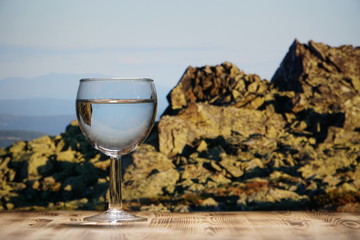 A glass glass glass with clean water stands on a wooden table against a mountain landscape.