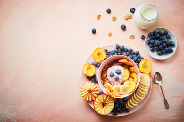Healthy breakfast bowl berry greek yoghurt with frefh blueberries, banana and flakes on the pink wooden table
