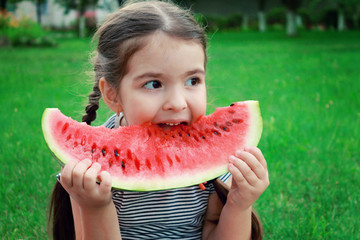 A girl is sitting on the lawn and eating a watermelon.