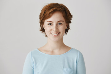 Friendly cute redhead european female colleague with freckles, smiling broadly, standing with...