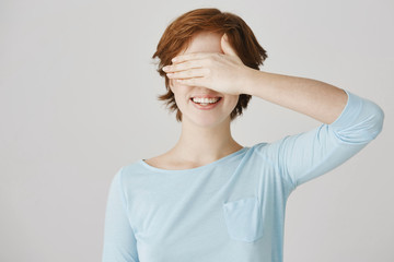 I promise not to look, lead me. Charming bright redhead female covering eyes with palm and smiling...