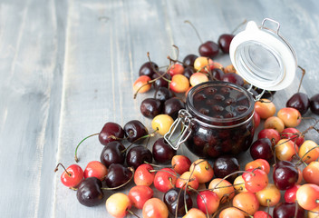 cherry marmalade ( cherry jam )  in a glass jar with a lid, a jar  stands among yellow and red cherries, conservation for the winter. selective focus and copy space