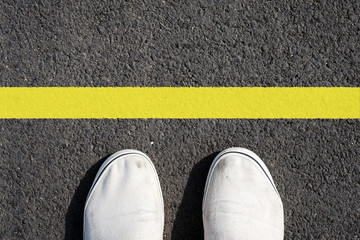 Two white sneakers on black asphalt. Yellow line. View from above. Copy space.