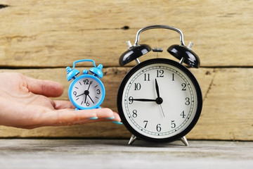 Woman holding a small blue alarm clock near a big one, on rustic wooden background