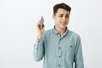 Portrait of displeased annoyed good-looking guy in casual outfit, pulling smartphone from ear with...