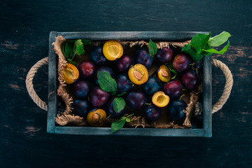 Plums with leaves in a wooden box. On a black wooden background. Top view. Free space for your text.